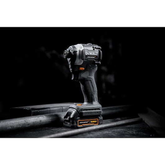 A DEWALT cordless impact driver, McLaren edition, is displayed upright on a dark industrial surface. The tool features black and orange accents and visible branding.