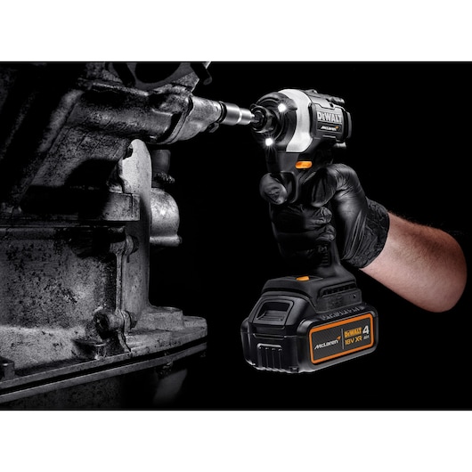 A gloved hand uses a DEWALT cordless impact wrench on a metal part. The tool is battery powered and illuminated.