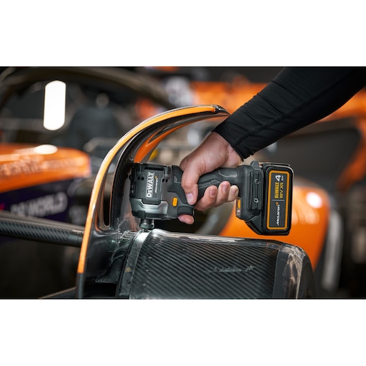 Person uses a DEWALT cordless drill on a carbon fiber part of an orange vehicle.