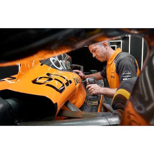 Person using a DEWALT tool on the side of an orange race car in a garage setting.