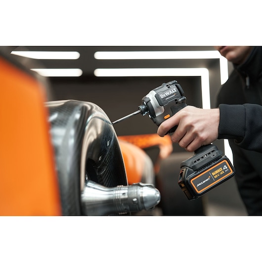 A person uses a DEWALT cordless impact driver on a metallic and carbon fiber surface beside orange details.