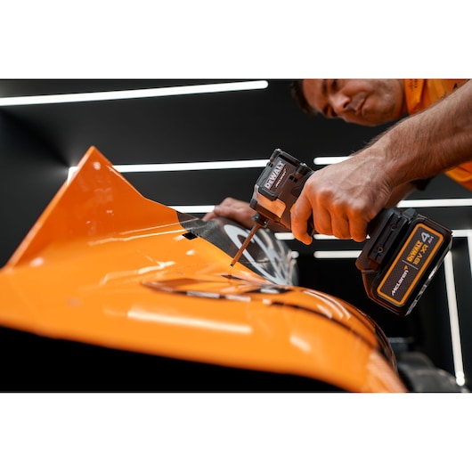 Person using a DEWALT cordless tool on an orange surface in a workshop setting.