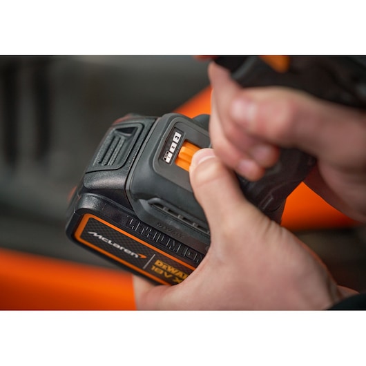 Close-up of hands holding a DEWALT 18V battery, showing the charge level indicator and McLaren branding.