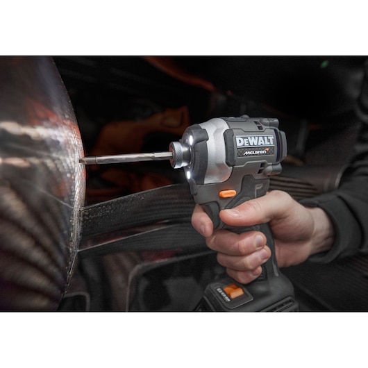 Hand holding a DEWALT cordless impact driver, drilling into a surface with LED light on.