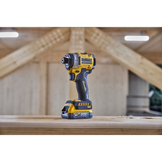 DEWALT cordless impact driver on a wooden surface inside a workshop with beams in the background.