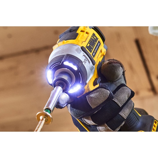 Close-up of a DEWALT cordless impact driver in use, LED lights illuminated, held by a gloved hand.