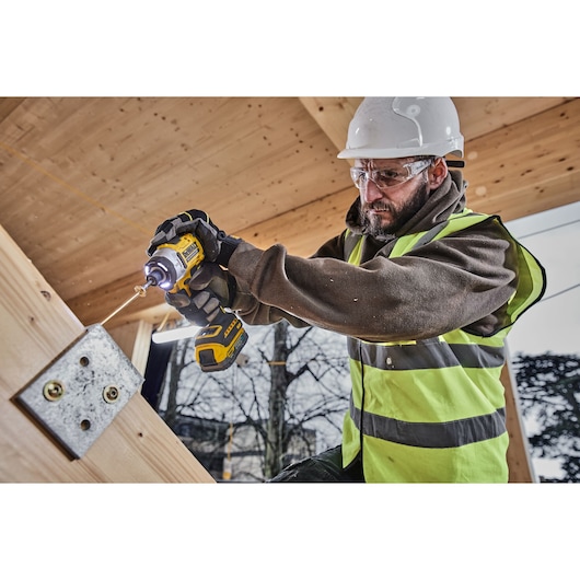 DEWALT DCK2201P1T1-XE and DCF860NT used by worker drilling into metal plate at construction site.