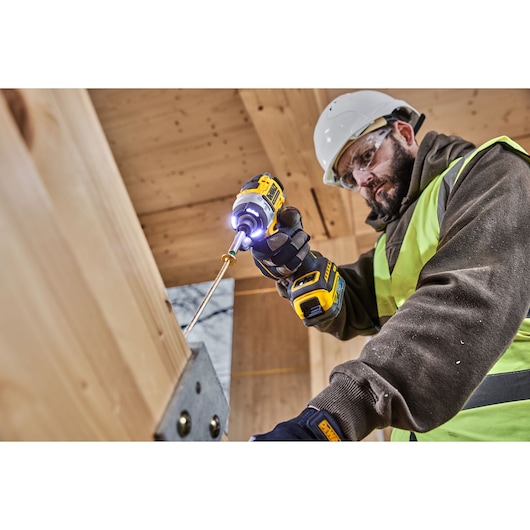 Worker uses DEWALT tools DCK2201P1T1-XE, DCF860NT for construction. Wearing helmet and vest.