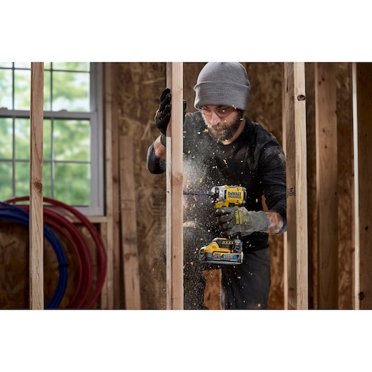 DEWALT DCK2201P1T1-XE and DCF860NT in use on wood framing, construction site, tool creates sawdust.