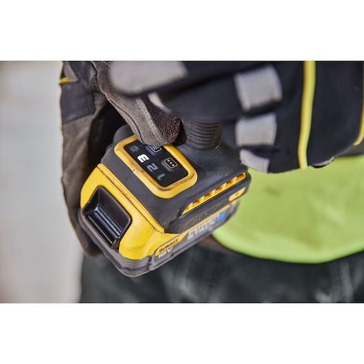 Gloved hand holds a DEWALT power tool with control buttons and yellow casing, close-up view.