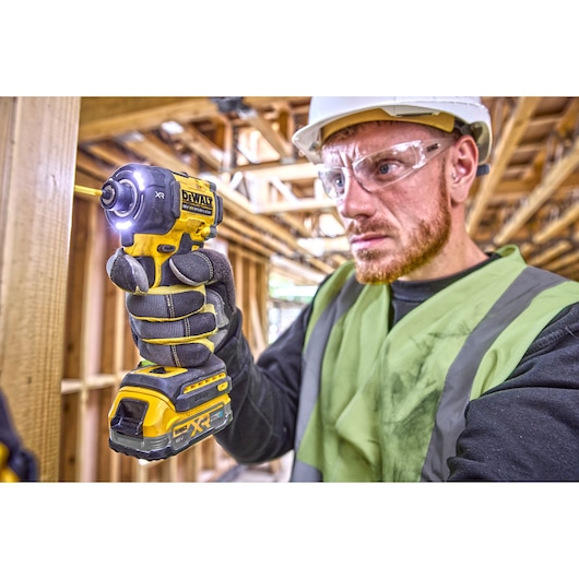 Worker using a DEWALT DCF870E2T impact driver with gloves at a construction site. Face is blurred for privacy.