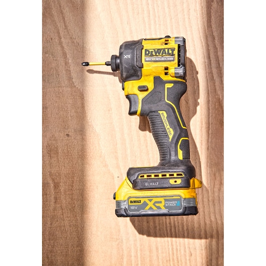 DEWALT 18V XR brushless impact driver placed on a wooden surface, showing its yellow and black design.