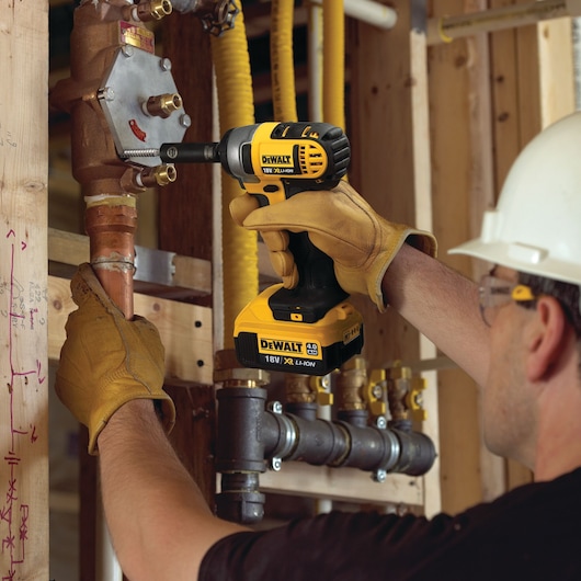 Gloved hand uses a DEWALT cordless impact driver on an orange stand in an industrial setting.