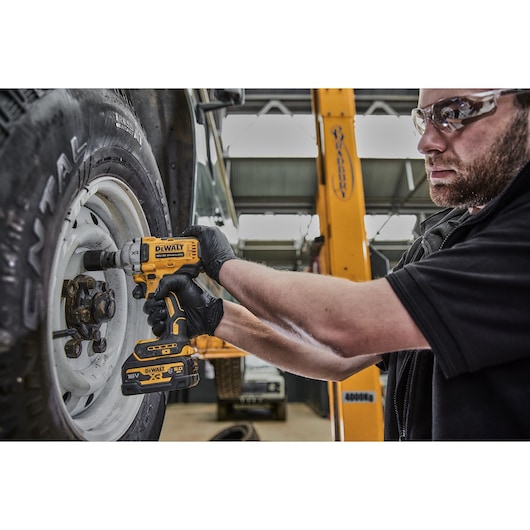 Person uses DEWALT DCF891NT impact wrench to tighten bolts on a vehicle wheel in a garage setting.
