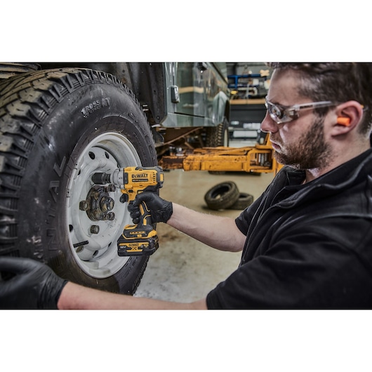 Person uses DEWALT cordless impact wrench to work on car wheel in a workshop.