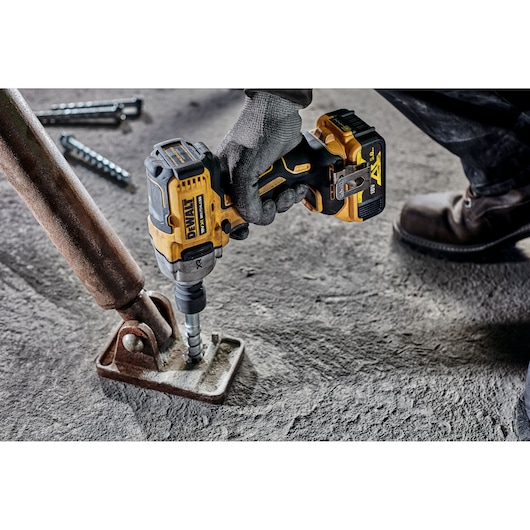Gloved hand using DEWALT cordless impact wrench on a metal bracket fixed to a concrete floor.