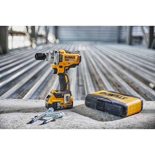 DEWALT cordless impact wrench, sturdy yellow case, and screws on a concrete surface in an industrial setting.