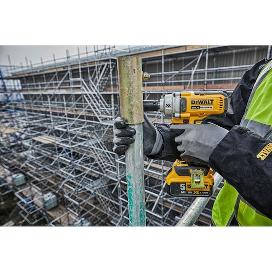 Worker using a DEWALT impact wrench on scaffolding outdoors at a construction site.