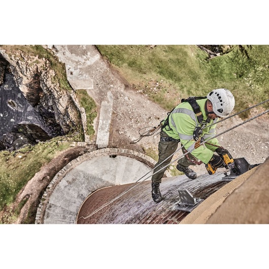 Worker uses DEWALT tool on harnessed climb, repairing structure outdoors above stone and grass area.