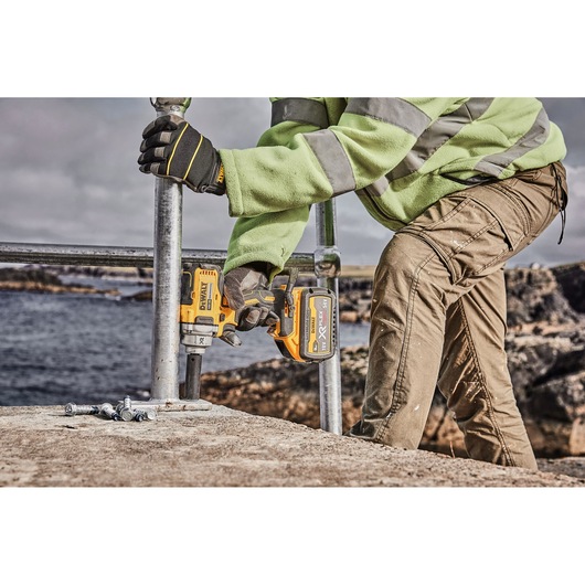 Person uses DEWALT cordless impact wrench DCF894P2 to secure bolts outdoors near water.