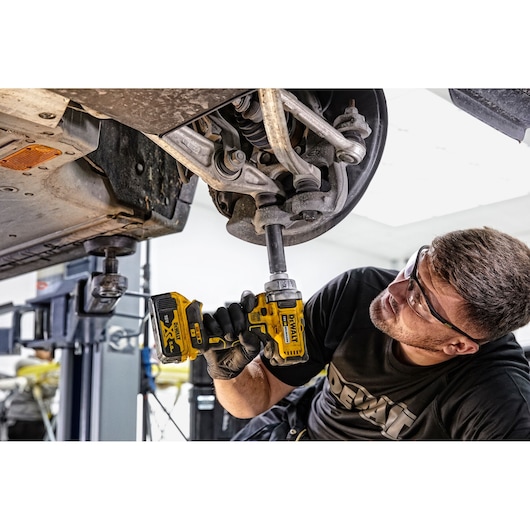 Person uses DEWALT DCF894P2 impact wrench on car suspension while working in a garage.