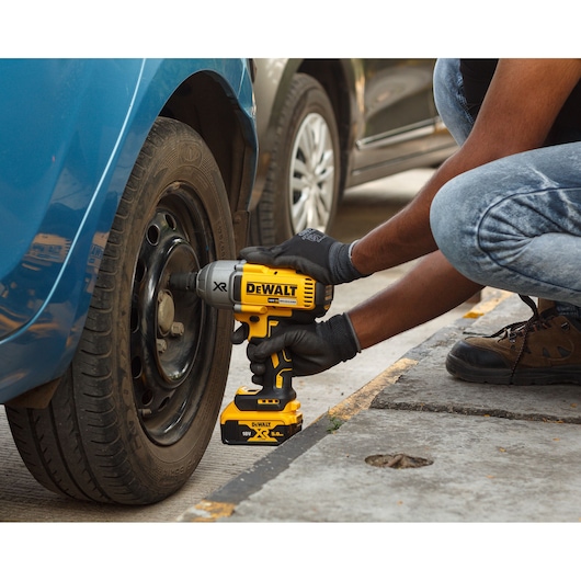Person uses DEWALT cordless impact wrench to tighten car wheel bolts outdoors.