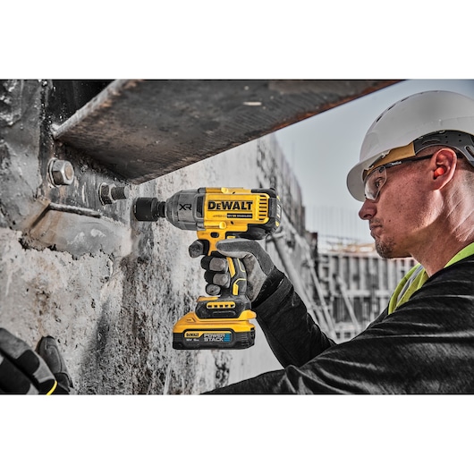 Worker uses DEWALT cordless impact wrench on a concrete structure at a construction site.