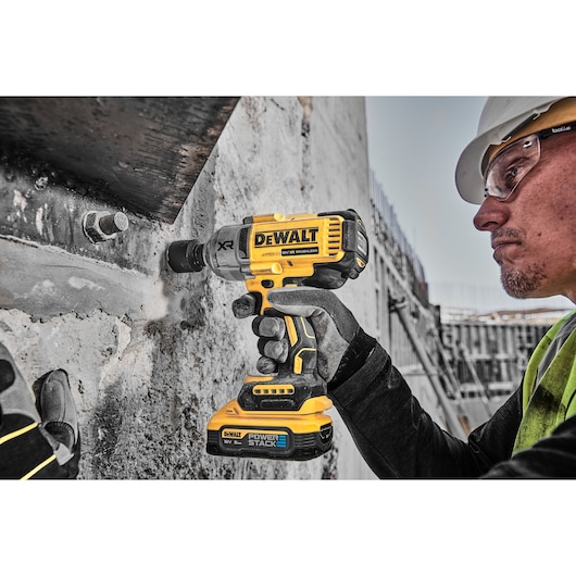 Worker using yellow DEWALT DCF900H2T impact wrench on concrete with gloves at construction site.