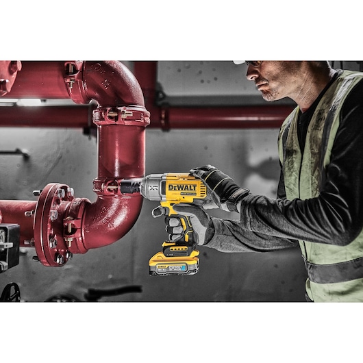 Person uses DEWALT DCF900H2T impact wrench on a red pipe in an industrial setting.