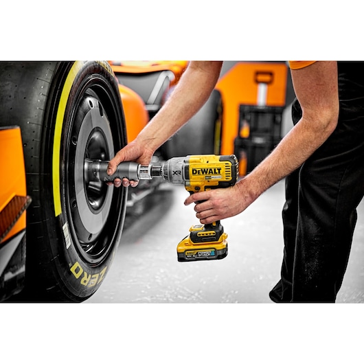 A person using a DEWALT DCF900H2T cordless impact wrench to work on the wheel of an orange racing car. The tool is being