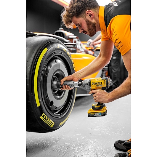 A person in an orange and black uniform uses a DEWALT DCF900H2T power tool to work on a Pirelli tire of a racing car. The