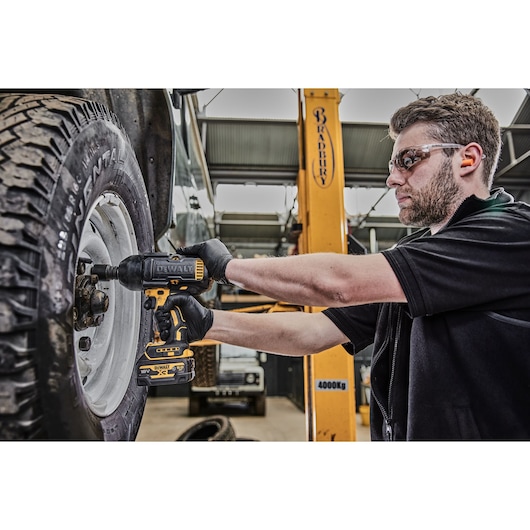 Person using a DEWALT DCF900P2G impact wrench to tighten wheel nuts on a vehicle inside a workshop.