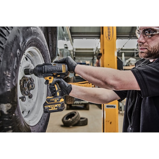 DEWALT impact wrench DCF900P2G used to tighten a wheel lug nut in an automotive workshop.