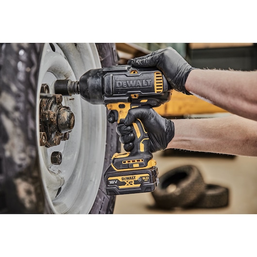 DEWALT cordless impact wrench loosening wheel nuts on a vehicle, used by a gloved hand.
