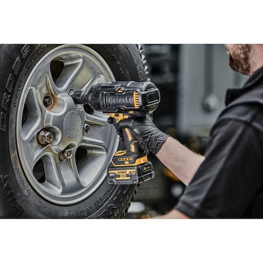 Person uses a DEWALT cordless impact wrench to tighten a lug nut on a car wheel.