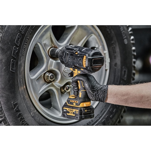 DEWALT cordless impact wrench used on a car wheel, held by a person wearing a black glove.