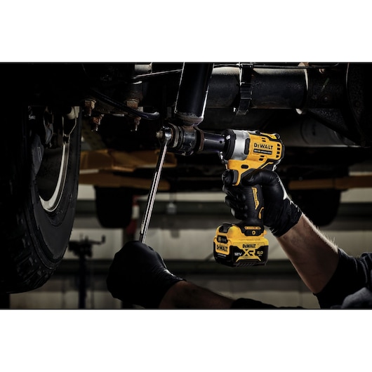DEWALT cordless impact wrench used on car undercarriage by gloved hands in a workshop.