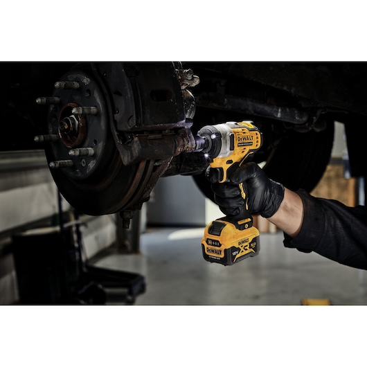 DEWALT cordless impact wrench being used on a car wheel by a gloved hand in a garage setting.