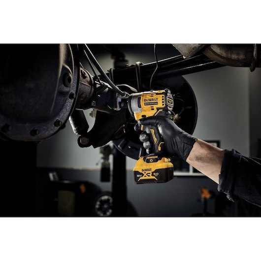Person uses DEWALT DCF901P1 impact wrench on vehicle part in workshop.