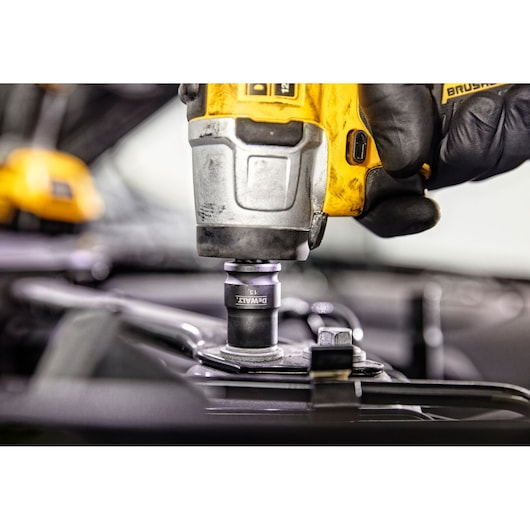 Close-up of a DEWALT cordless impact wrench being used, held by a gloved hand, tightening a bolt on a piece of metal equipment.