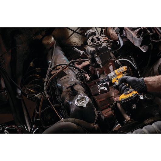 A person wearing a black glove is using a DEWALT DCF902D2 cordless impact wrench to work on an engine inside a vehicle.