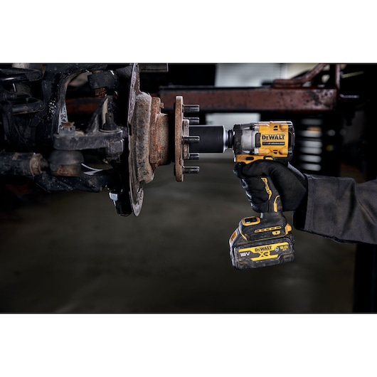 A person using a DEWALT cordless impact wrench (model DCF921P2G) to remove or tighten lug nuts on a vehicle wheel hub.