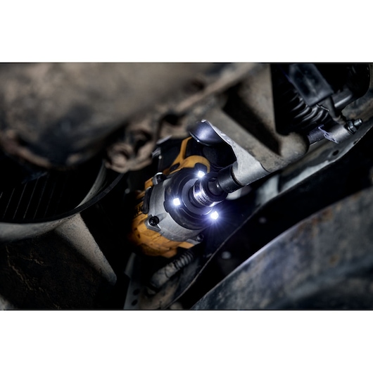 Close-up of a DEWALT cordless impact wrench with LED lights, being used to work on a vehicle in a dimly lit area.