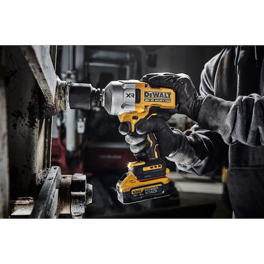 DEWALT cordless impact wrench in use by gloved hands on metal machinery in an industrial workshop.
