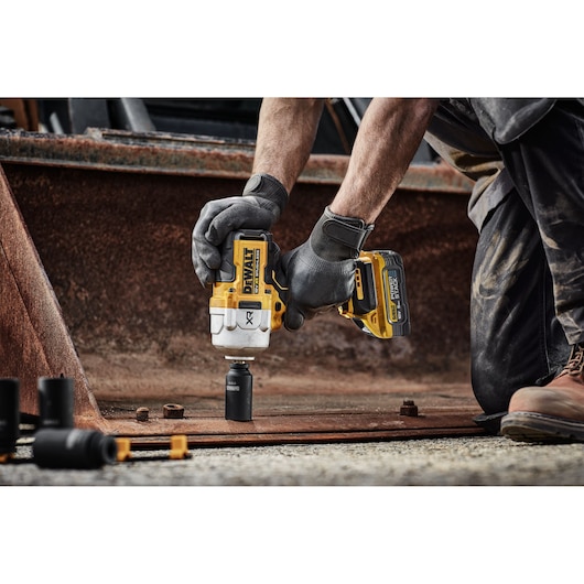 A DEWALT DCF961H2T impact wrench in use on rusty metal, held by a person wearing gloves outdoors.