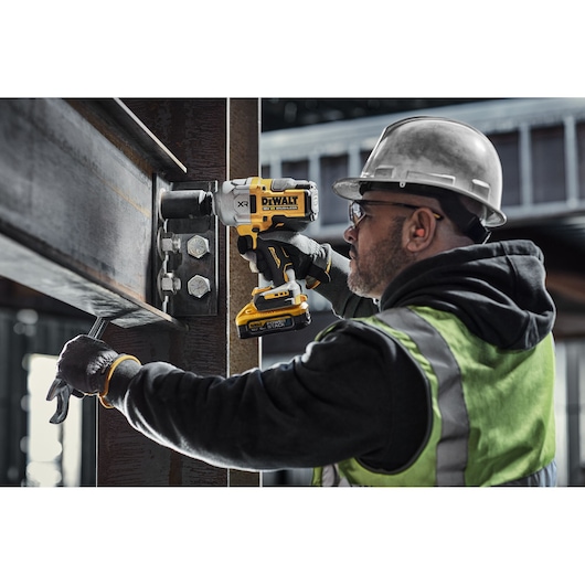 Person uses DEWALT impact wrench to tighten bolts on steel beam at a construction site.