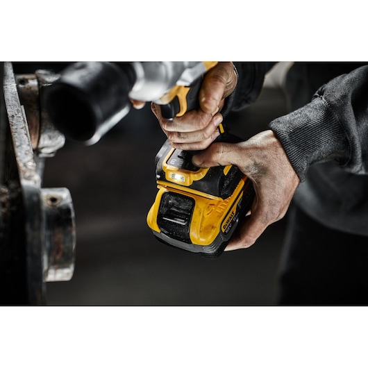 Person operating a yellow DEWALT cordless tool, focusing on handle and battery in a workshop setting.