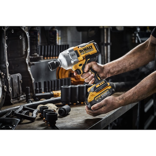 Person holding a DEWALT impact wrench on a workbench with sockets and tools nearby.