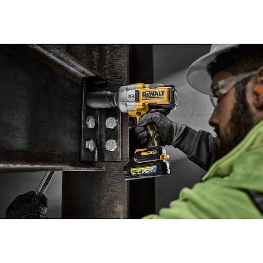Worker using DEWALT cordless impact wrench on steel beam bolts at a construction site.