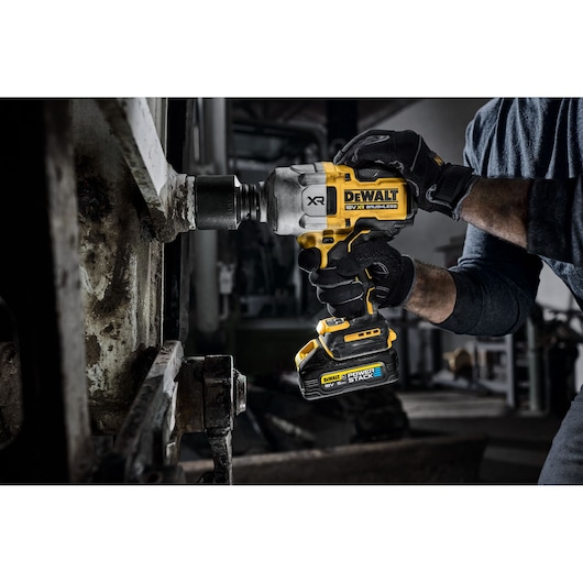 Hand using DEWALT cordless impact wrench on metal machinery in workshop setting.